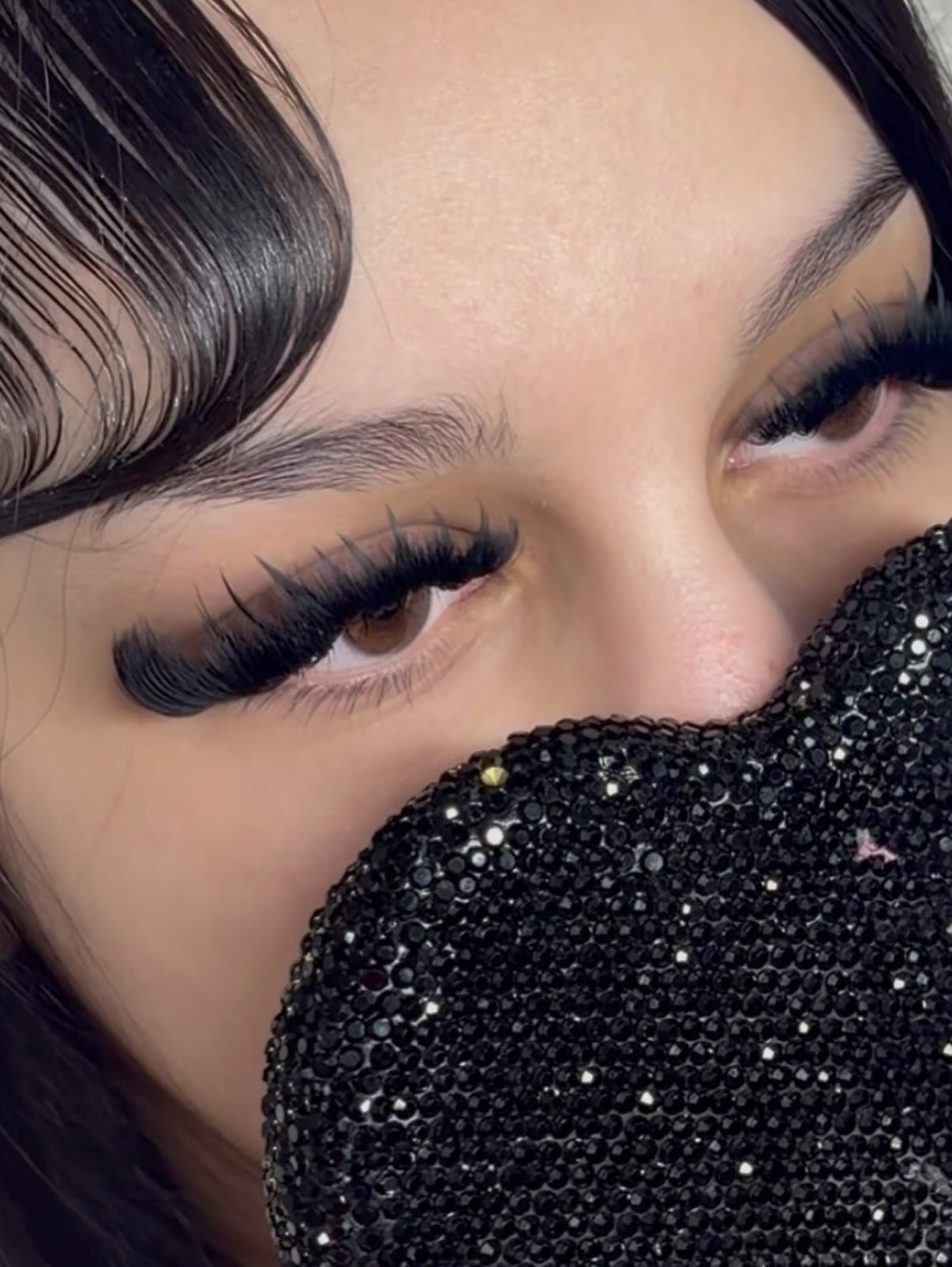 Close up of a full lash set, with the signature black rhinestone heart held over the client's face