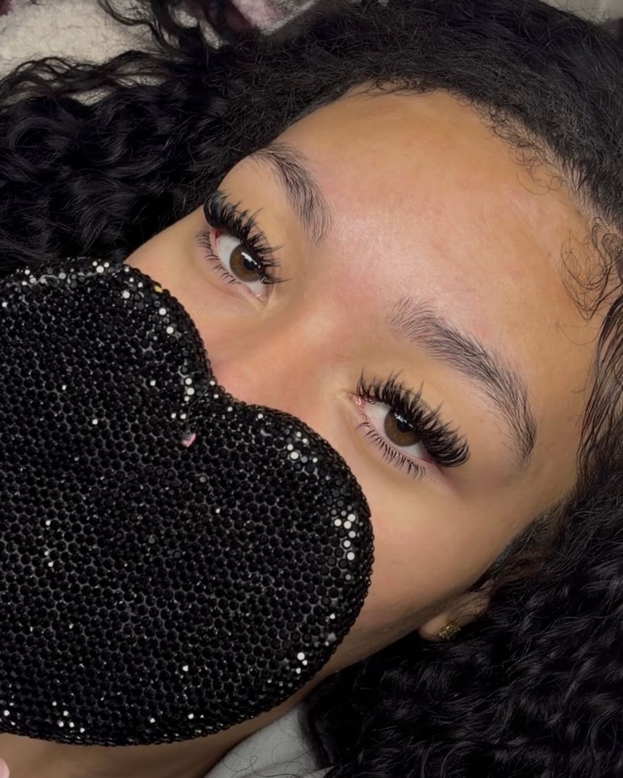 Full lash set on a client with curly hair, black heart held over the face